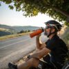 hydrate-cyclist Cyclist sipping an orange sports drink from a plain stainless steel bottle