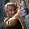 Active senior man in his 60s rock climbing on a natural cliff.